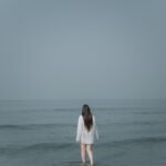 a woman standing in the ocean looking at the horizon