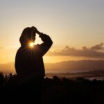 A man standing on top of a hill looking at the sun