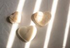 Three heart-shaped candles with textured designs basking in soft sunlight on a minimalist surface.