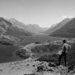 a man standing on top of a mountain next to a lake