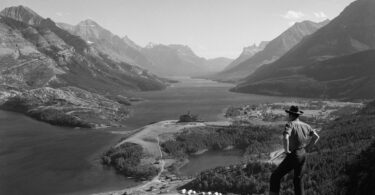 a man standing on top of a mountain next to a lake