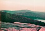 A man standing on top of a mountain next to a lake