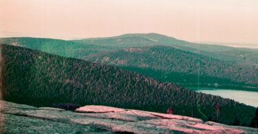 A man standing on top of a mountain next to a lake
