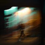 Blurred figure walking in front of a bright wall.