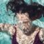 A woman swims underwater with bubbles.