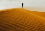 A lone figure stands on a sand dune at sunset.