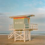A pastel colored lifeguard station on a sandy beach.